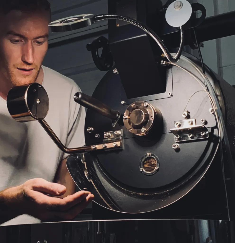 Male coffee roaster examines beans next to machine